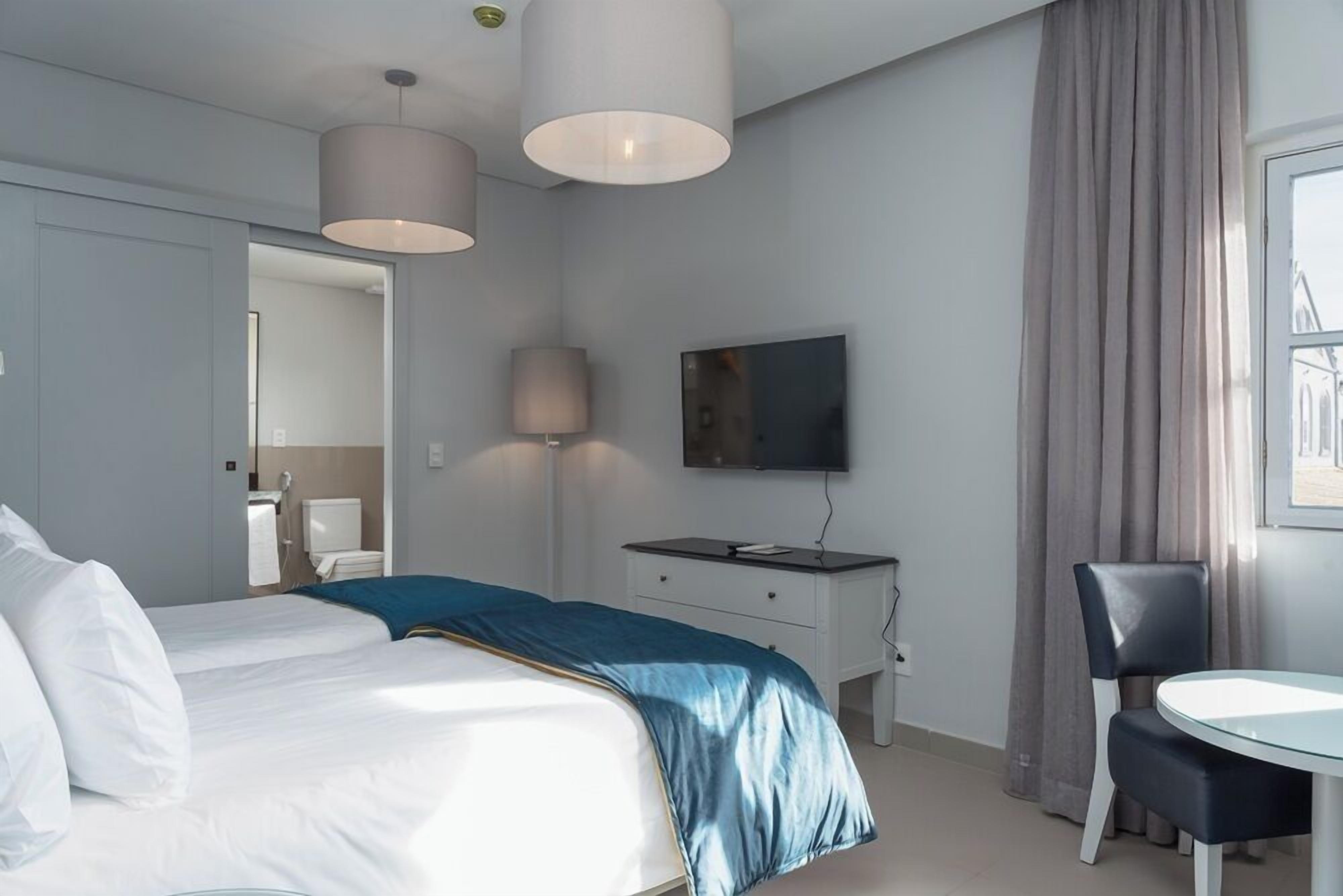 Una habitación de hotel moderna con una cama grande, un escritorio con silla, un televisor y una ventana con cortinas.