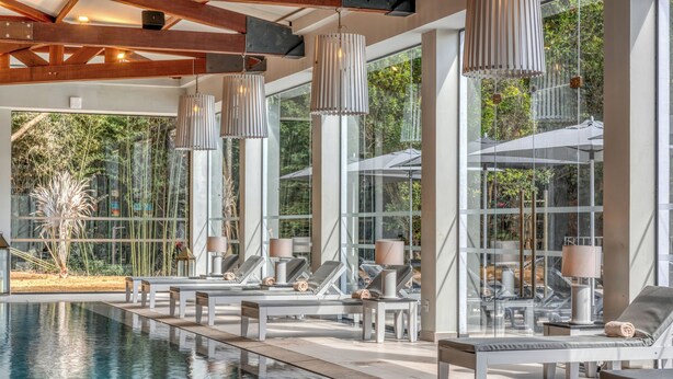 Un espace aménagé au bord de la piscine, avec des chaises longues, une piscine et de grandes fenêtres offrant une vue sur la verdure.
