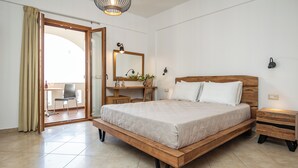 A bedroom with a wooden bed, a desk with a mirror, a chair, and a small table with a plant. - KALLISTI STUDIOS (Naxos)