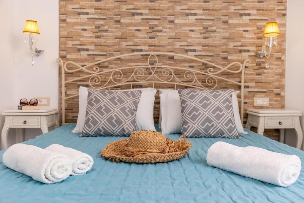 A neatly made bed with a blue bedspread, two pillows with geometric patterns, and a woven basket.