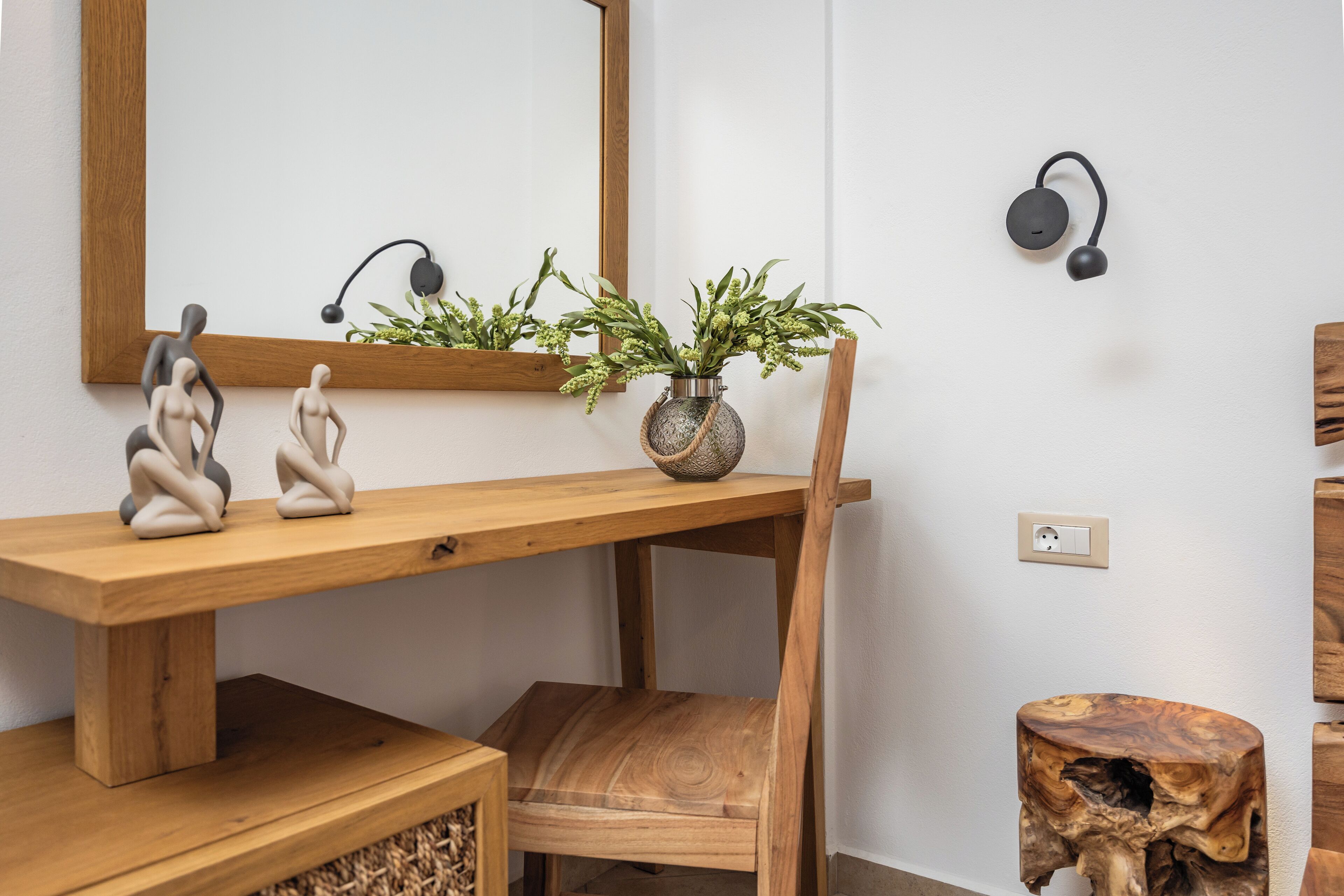 A wooden console table with a vase of green plants, two abstract sculptures, and a wooden chair.