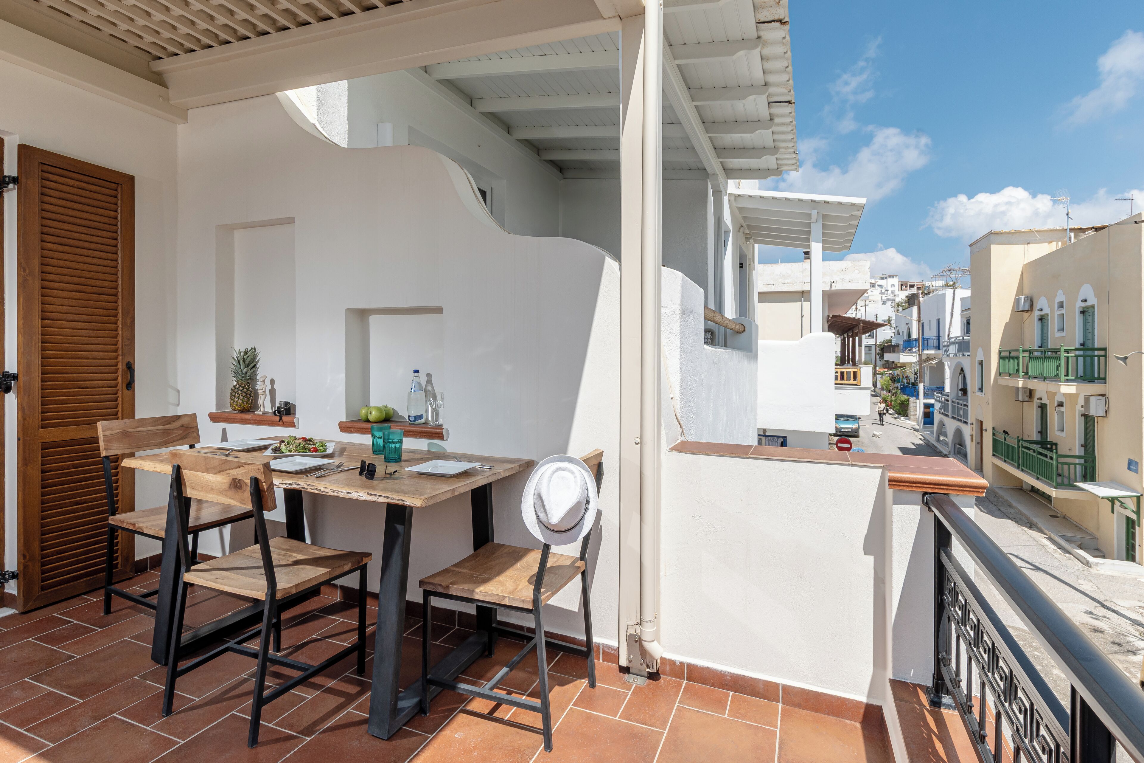 A balcony with a wooden table and chairs, a white chair, and a view of the street below.