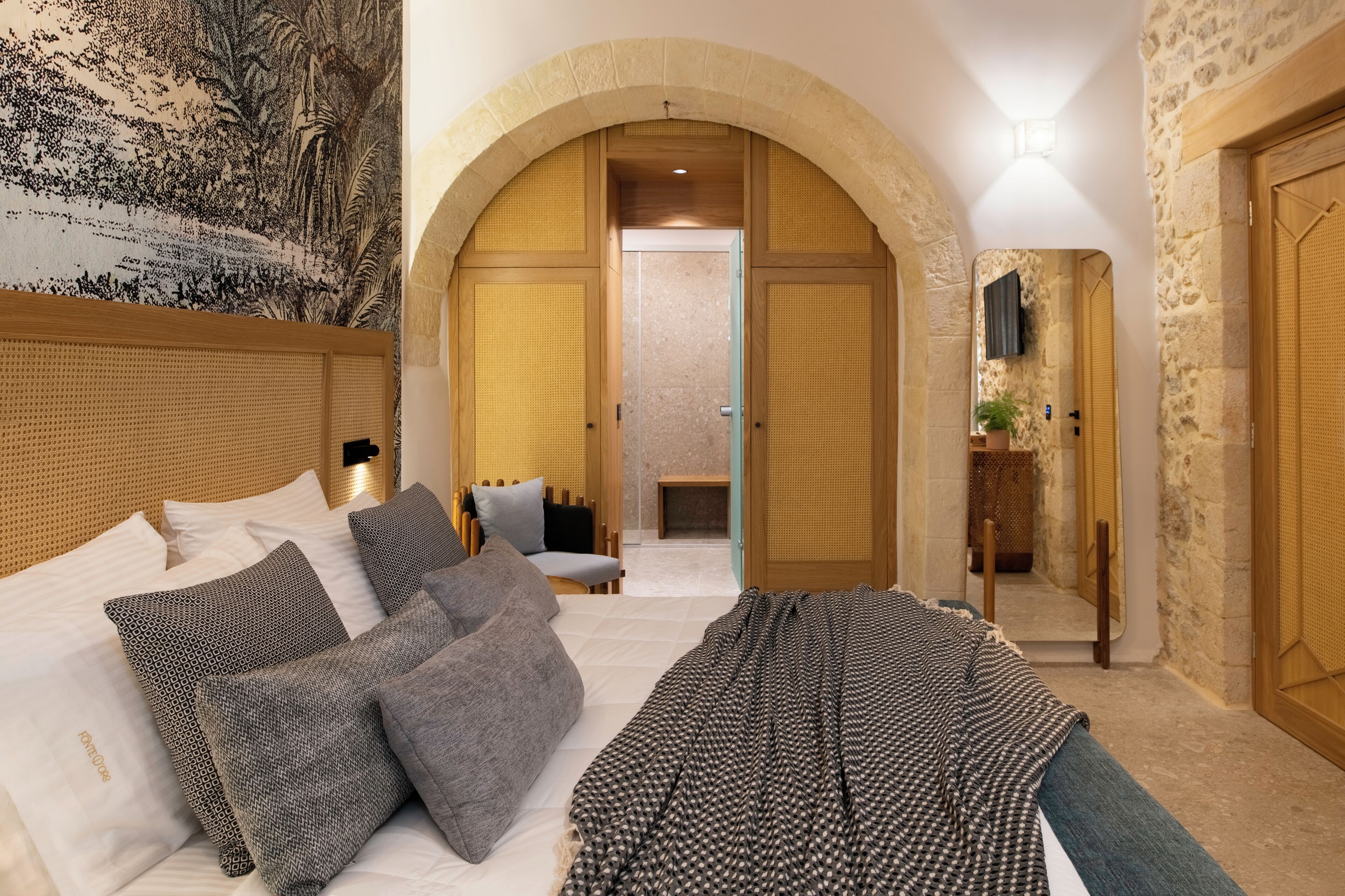 A hotel room with a large bed, a wooden headboard, a tapestry, and a stone wall.