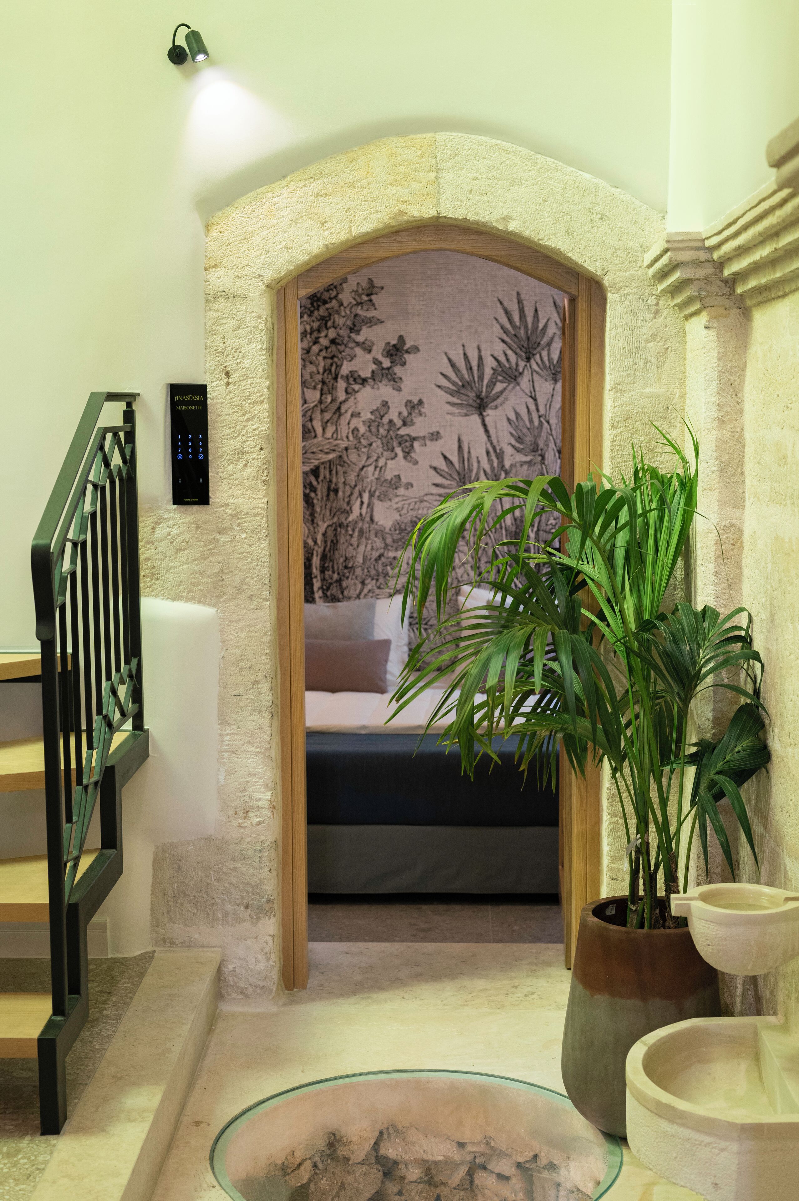 A staircase with a handrail, a wall-mounted light fixture, a potted plant, and a decorative wall panel.