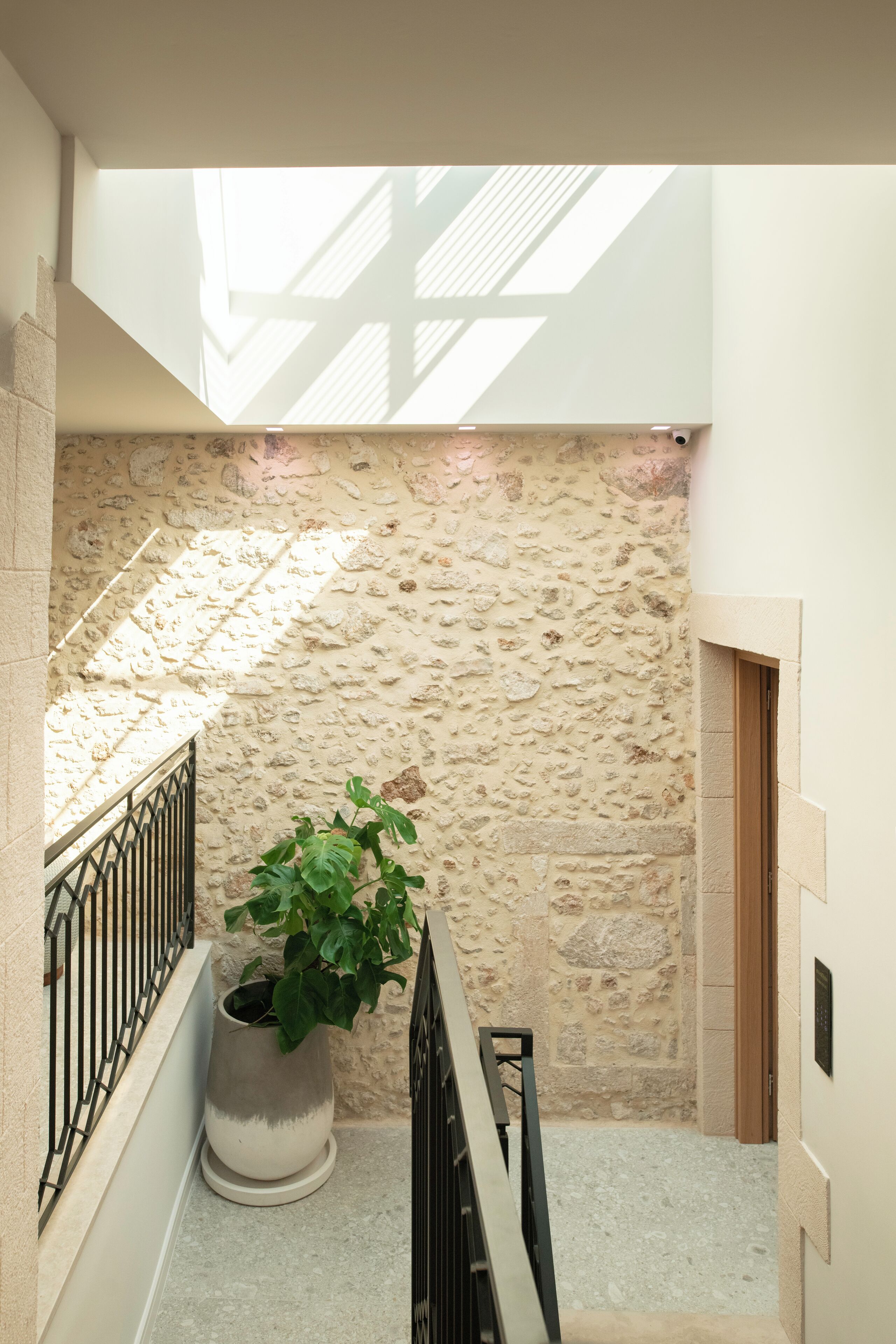 A narrow stairwell with a stone wall, a potted plant, and a metal railing.