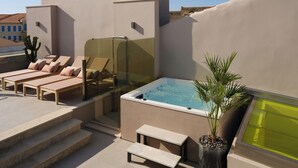 Une terrasse sur le toit équipée de chaises longues, d’un jacuzzi et d’un palmier.