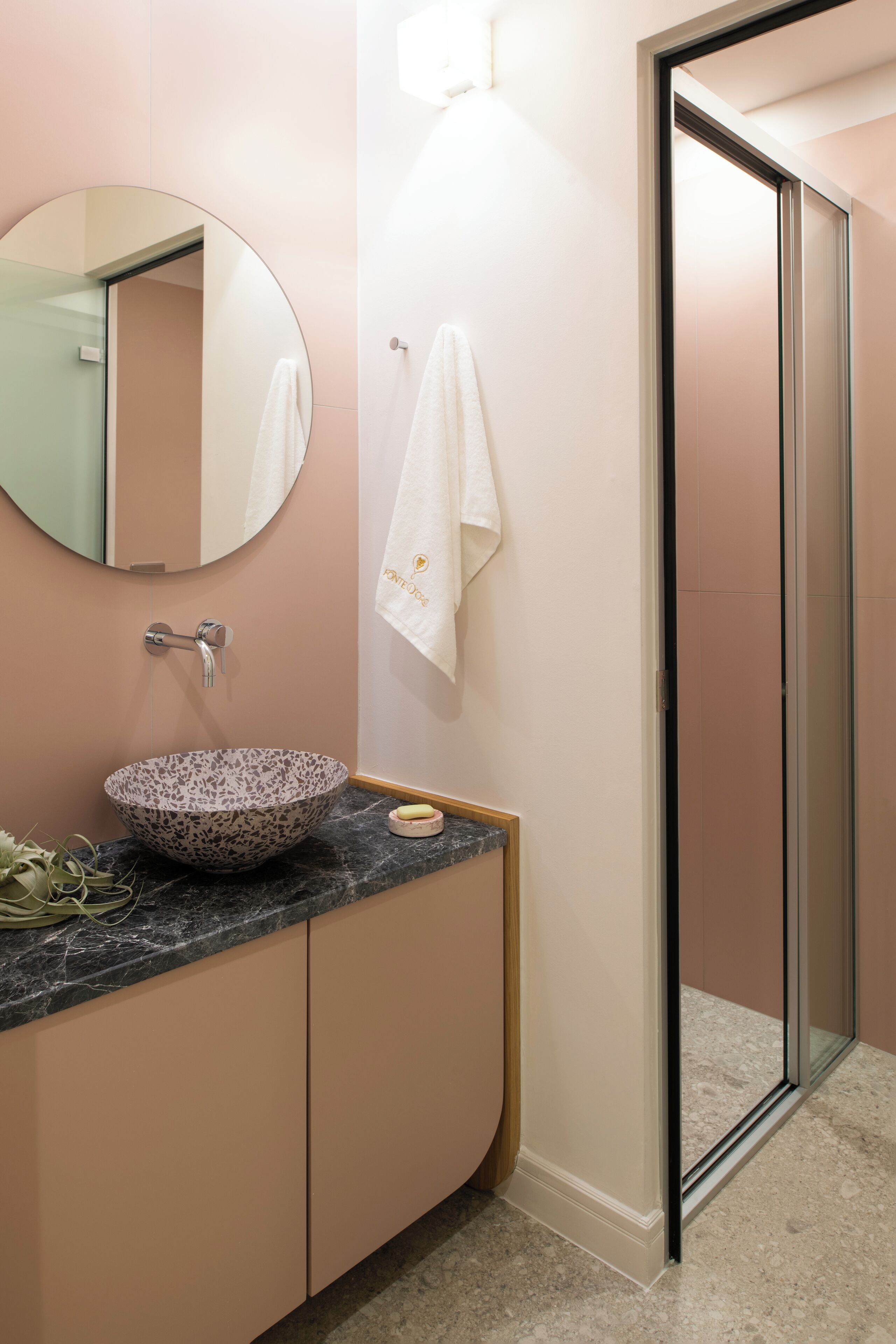 Un baño con un espejo redondo, un lavabo sobre encimera, una toalla colgada en la pared y una zona de ducha.