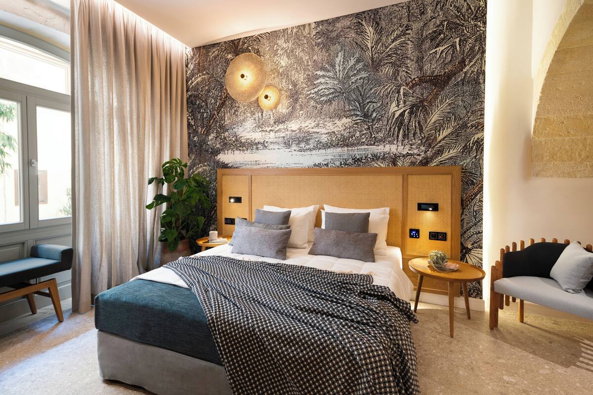 Un dormitorio con una cama grande, una mesita de noche, una silla, un escritorio y una pared con un mural de temática natural.