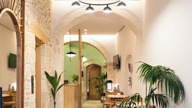 Un hall d’hôtel avec un mur en pierre, un comptoir d’accueil en bois et une table ronde entourée de chaises.