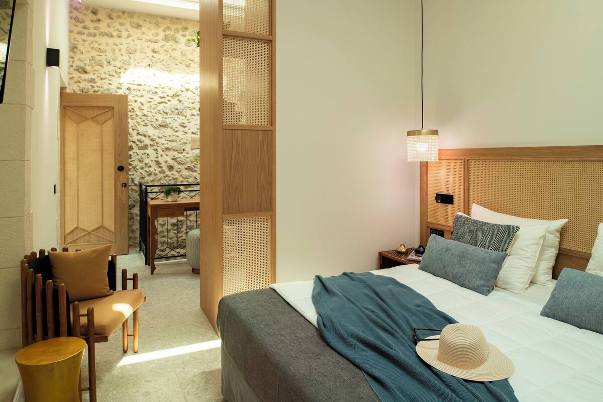 Un dormitorio con cama, mesita de noche, cabecero de madera y una zona de estar con una silla y una pequeña mesa.