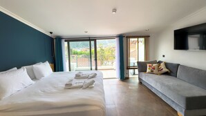 A hotel room with a large bed, a sofa, a TV, and a balcony with a view of the city.