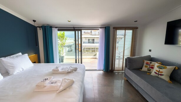 A hotel room with a bed, a sofa, a TV, and a balcony with a view of buildings.