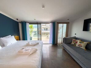 A hotel room with a bed, a sofa, a TV, and a balcony with a view of buildings. - Nakas Hotel (Fethiye)