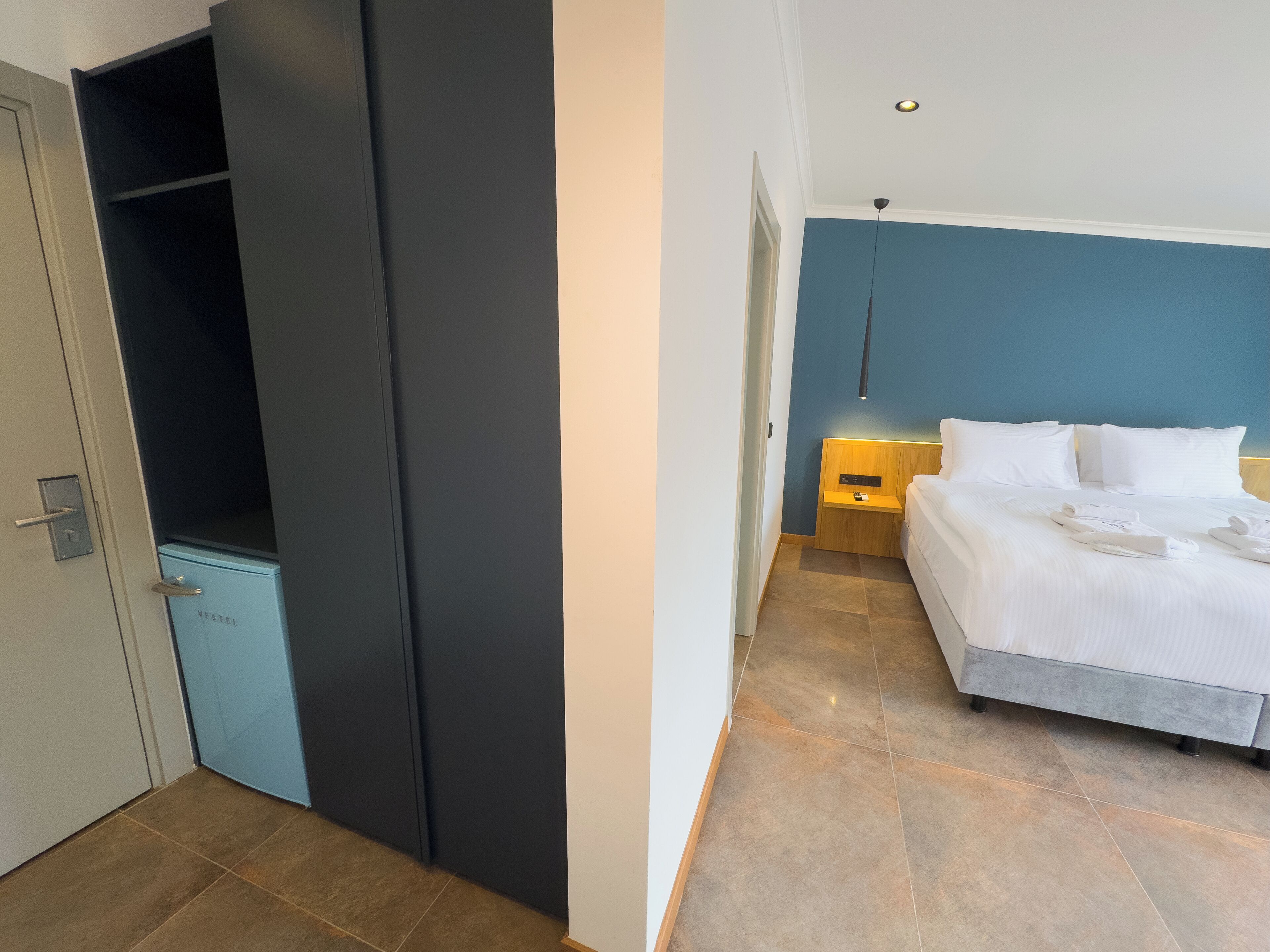 Een hotelkamer met een bed, nachtkastje, kledingkast en een deur.