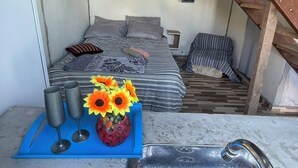A bedroom with a bed, pillows, a bedside table with a vase of flowers, and a striped blanket. - Alto da Colina Kitnetes - Penedo (RJ) (Penedo Itatiaia)