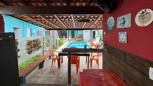A covered outdoor area with a pool, wooden benches, and orange chairs. - Alto da Colina Kitnetes - Penedo (RJ) (Penedo Itatiaia)