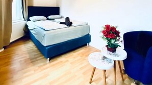 Een slaapkamer met een bed, een nachtkastje met een bloevas, een blauwe stoel en een raam met gordijnen.