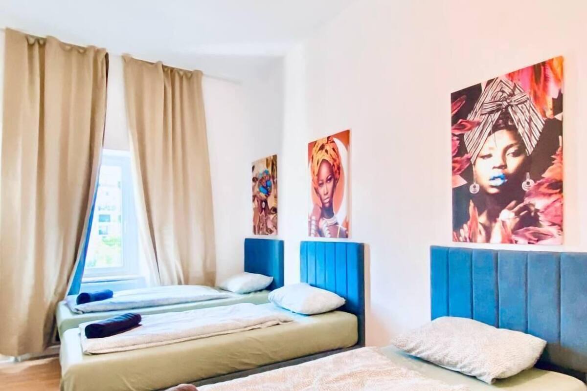 A room with two beds, beige curtains, and artwork on the walls.