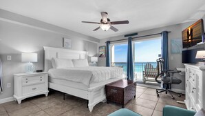 Ein Schlafzimmer mit Bett, Schreibtisch, Stuhl, Kommode, Deckenventilator und Meerblick.