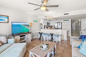 Una sala de estar con televisor, ventilador de techo, comedor y cocina al fondo, además de un pasillo que conduce a otras habitaciones.
