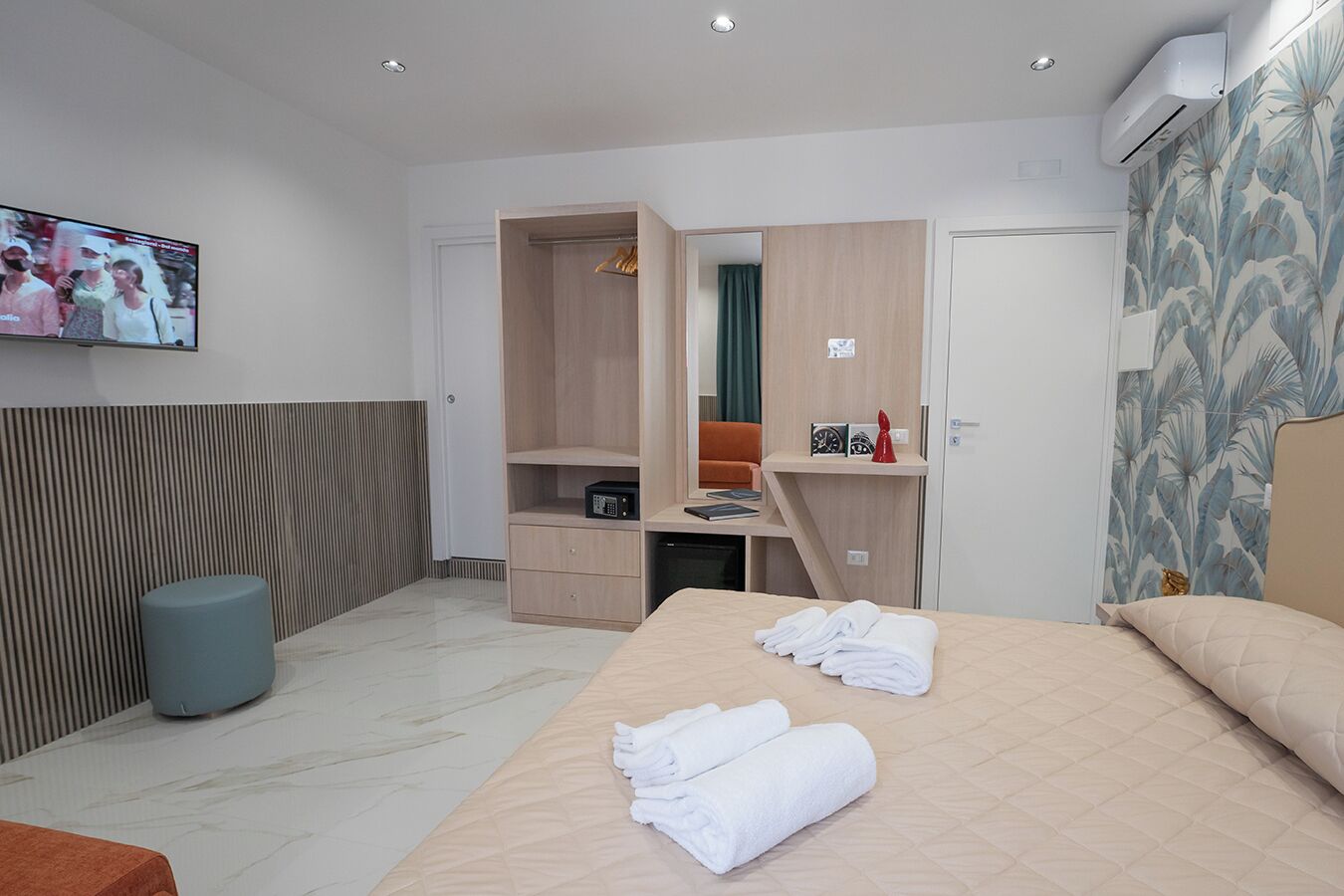 A modern hotel room with a bed, a desk, a wardrobe, and a television.