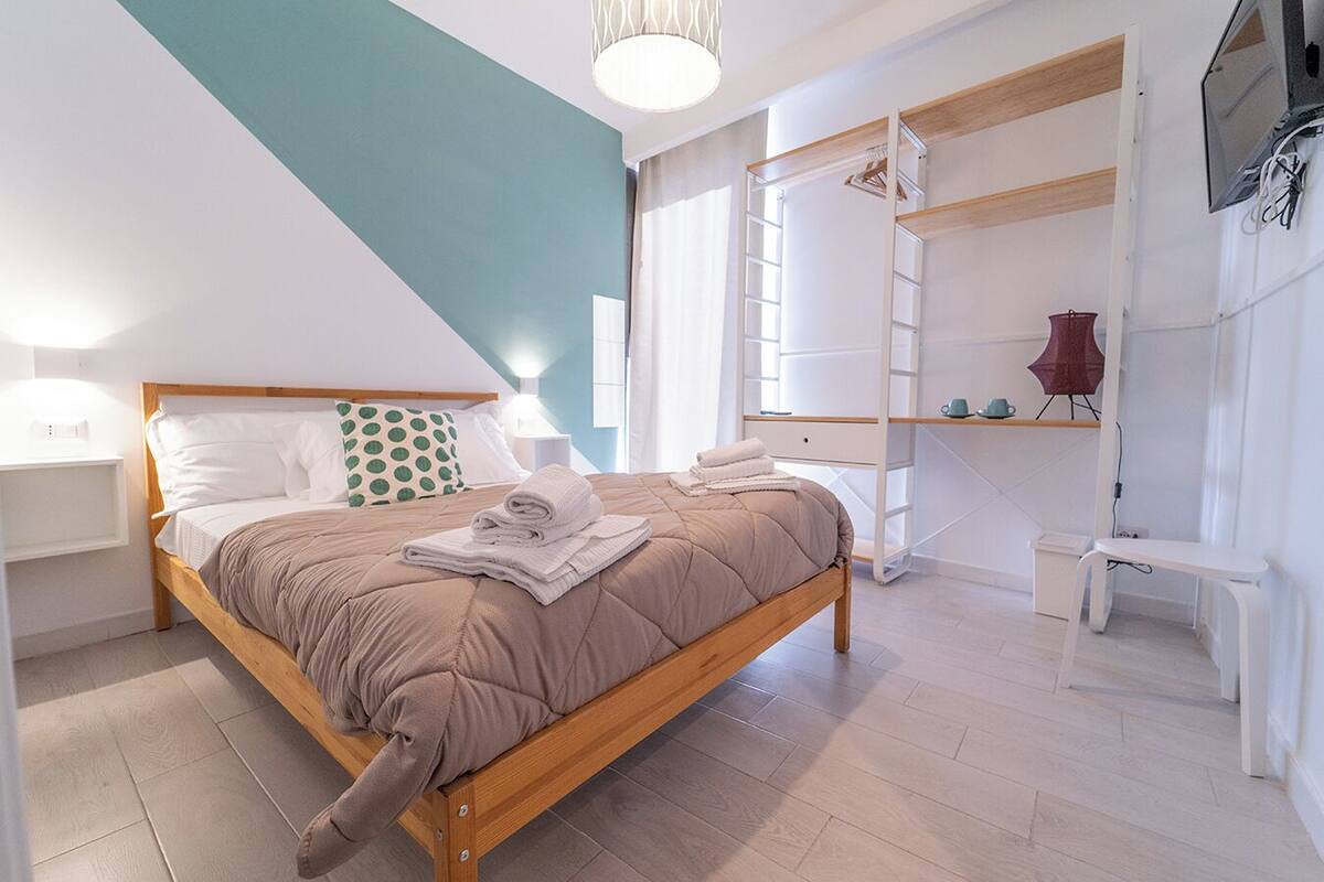 A modern bedroom with a wooden bed, a built-in wardrobe, and a TV mounted on the wall.
