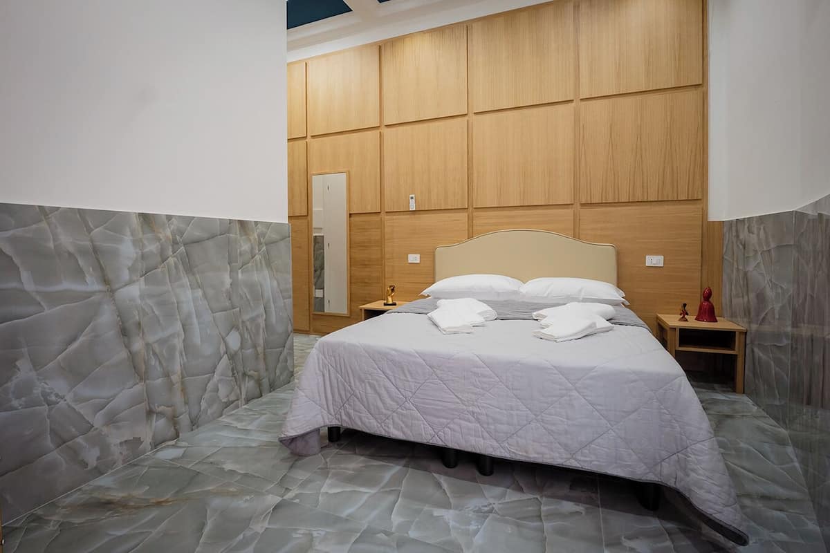 A hotel room with a bed, a nightstand, a mirror, and a wooden panel wall.