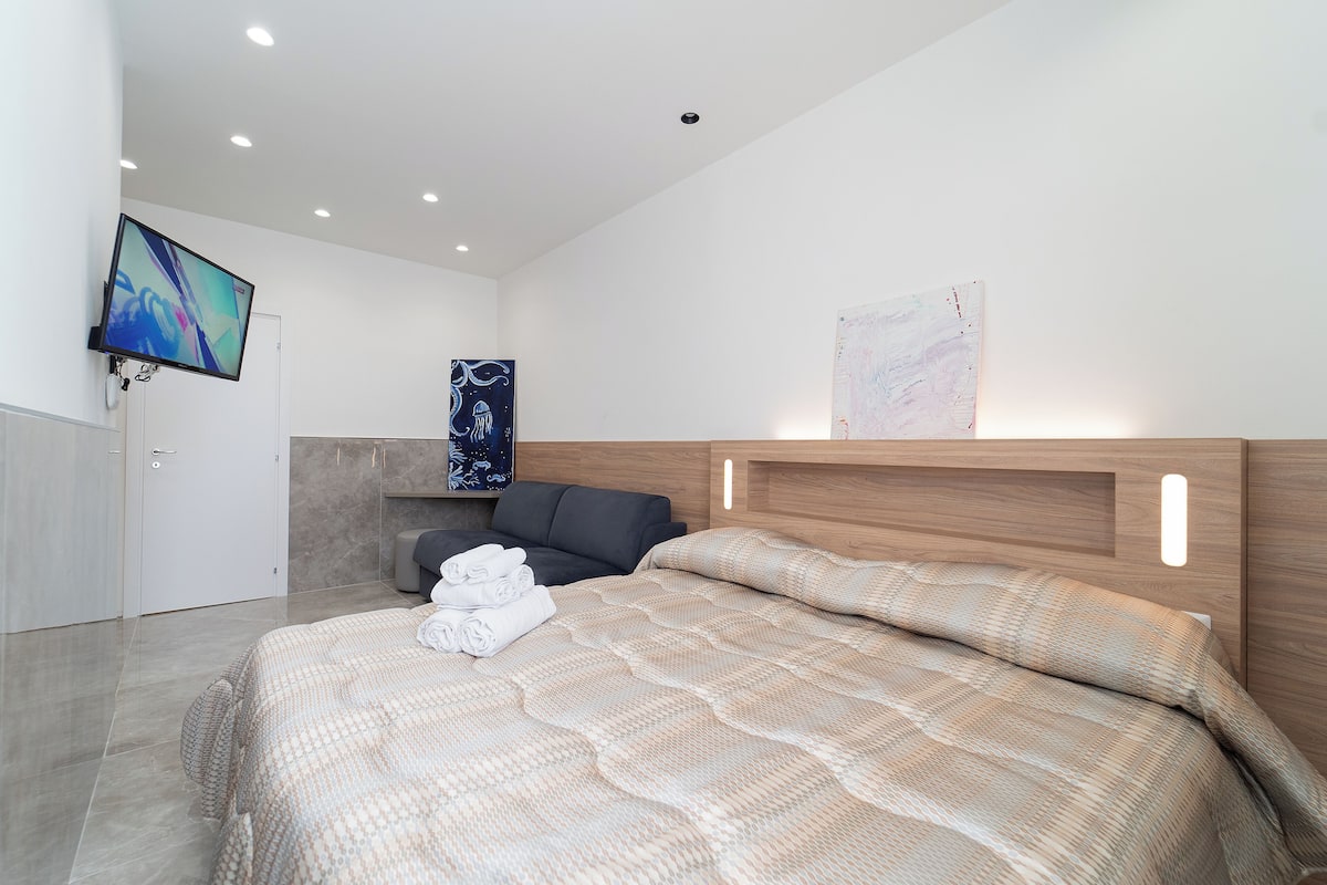 A modern bedroom with a large bed, a flat-screen TV mounted on the wall, and a wooden headboard.