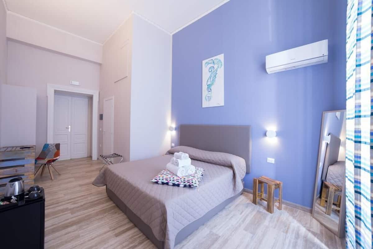 A bedroom with a bed, a bedside table, a chair, a desk, and an air conditioning unit.