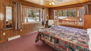 Un dormitorio de cabaña de madera con una cama, una silla y ventanas grandes.