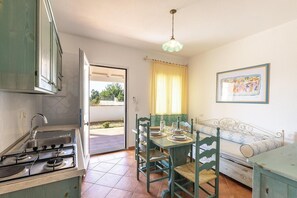 A kitchen with a stove, sink, and dining table with chairs. There is a window with curtains and a painting on the wall.