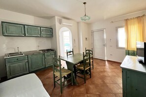 A compact kitchen with a dining table and chairs, a built-in stove, and a single window with curtains.