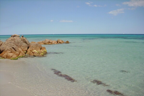 A beach with clear turquoise water and large rocks.