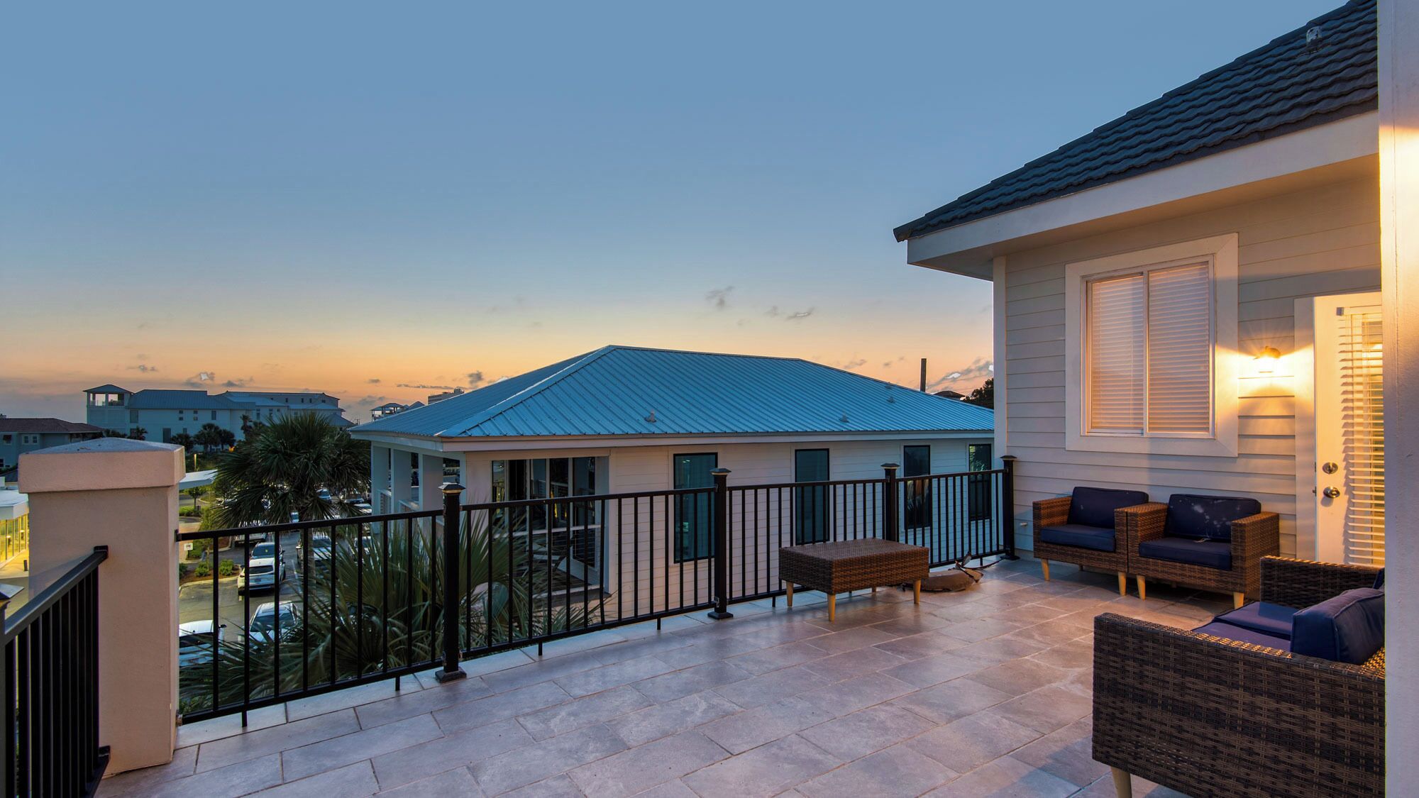 A balcony with wicker furniture and a view of a building with a blue roof.