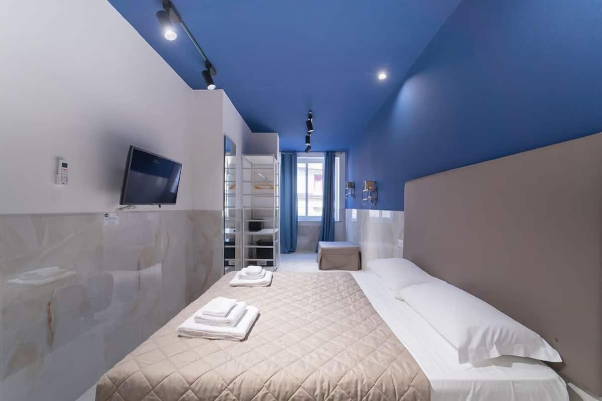 A modern hotel room with a bed, a TV, a wardrobe, and a bathroom with a mirror and towel rack.