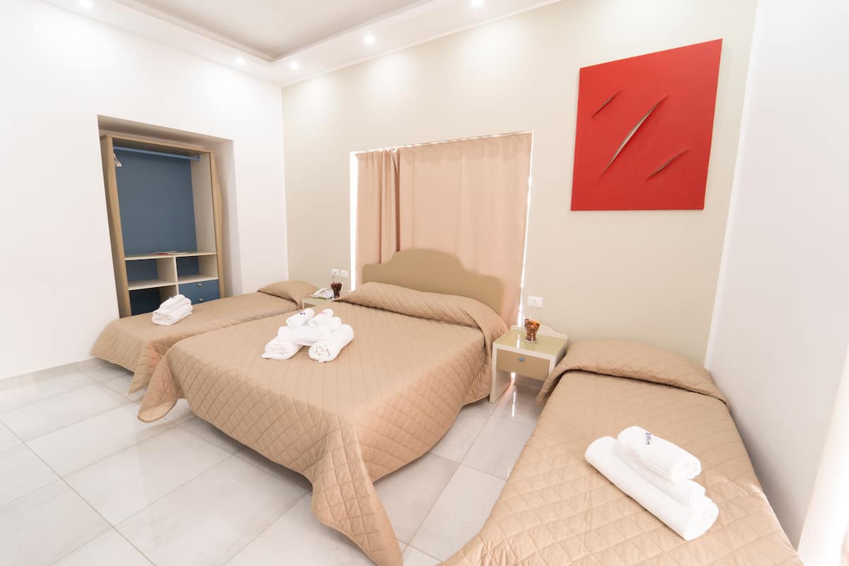 A hotel room with two beds, a wardrobe, a bedside table, and a red artwork on the wall.