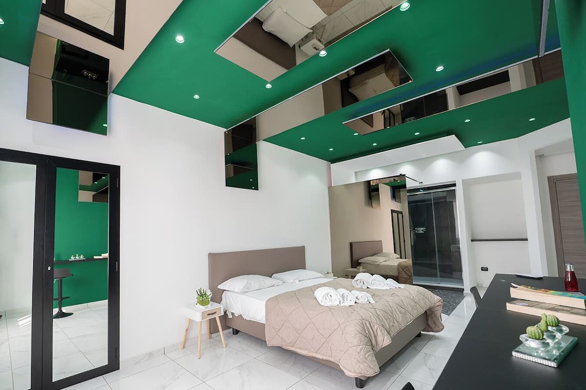 A modern hotel room with a large bed, a separate shower area, and a dining table with books and a cactus.