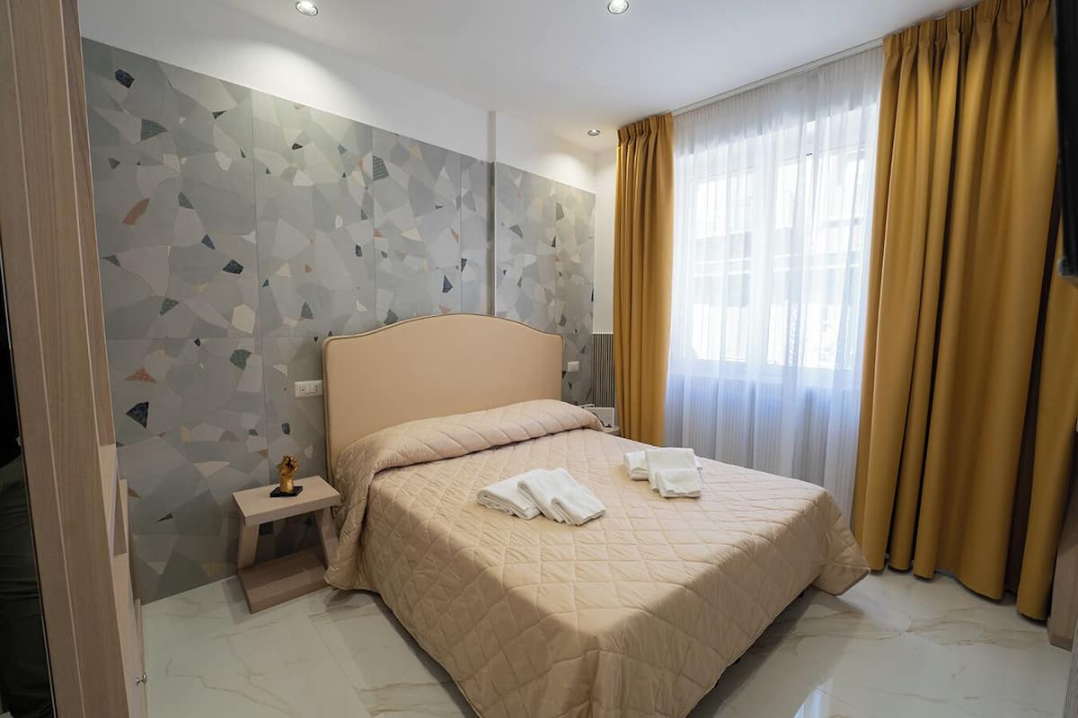 A hotel room with a bed, a nightstand, a decorative item, and a window with curtains.