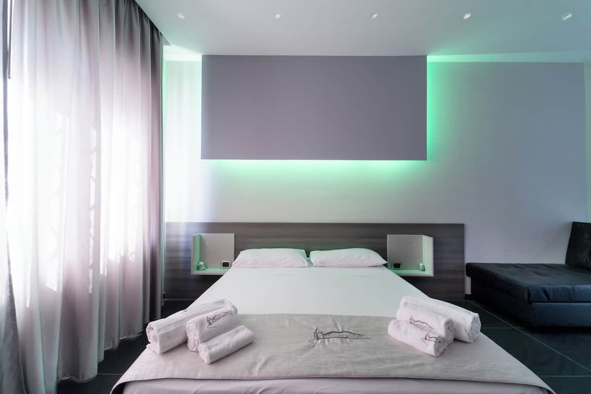 A modern hotel room with a large bed, a flat-screen TV mounted above it, and a bedside table with a lamp.