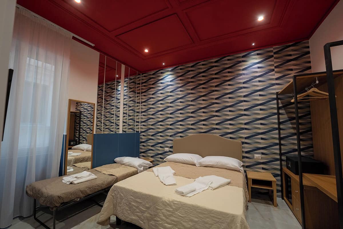 A hotel room with two beds, a mirror, a wardrobe, and a patterned wall.