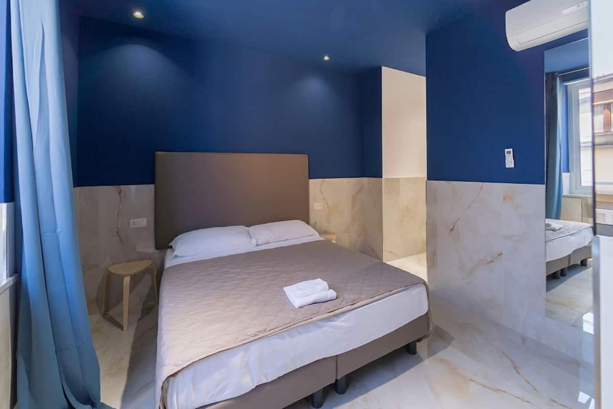A modern hotel room with a large bed, a small stool, and a bathroom with a mirror and sink.