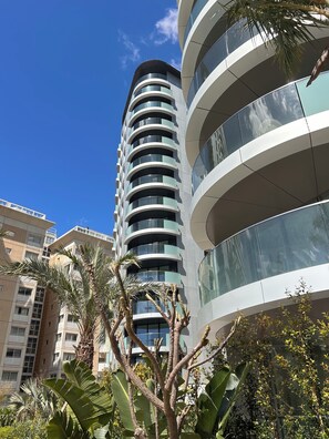 A modern high-rise building with multiple balconies, surrounded by tropical vegetation. - EuroCity by Bentley Holiday Apartments (Pool, Gym & Parking) (Gibraltar)