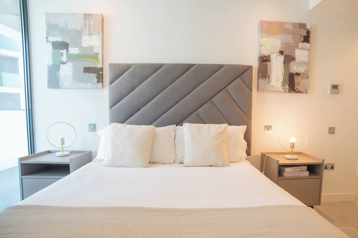 A modern hotel room with a large bed, two bedside tables, and abstract art on the walls.