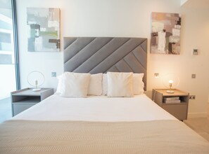Une chambre d’hôtel moderne avec un grand lit, deux tables de chevet et des œuvres d’art abstraites accrochées aux murs.