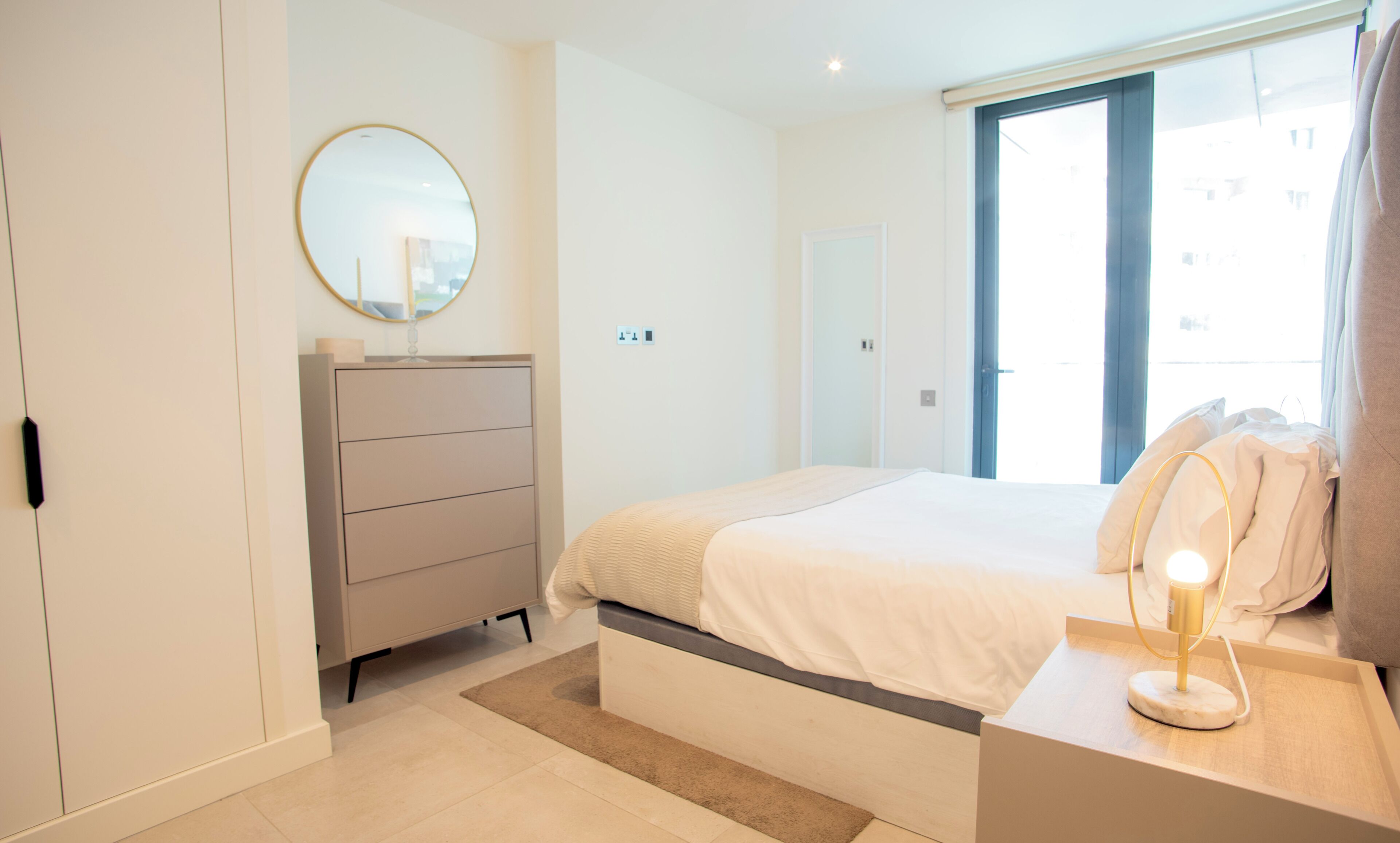 Een slaapkamer met een bed, dressoir, spiegel en bedlampje.