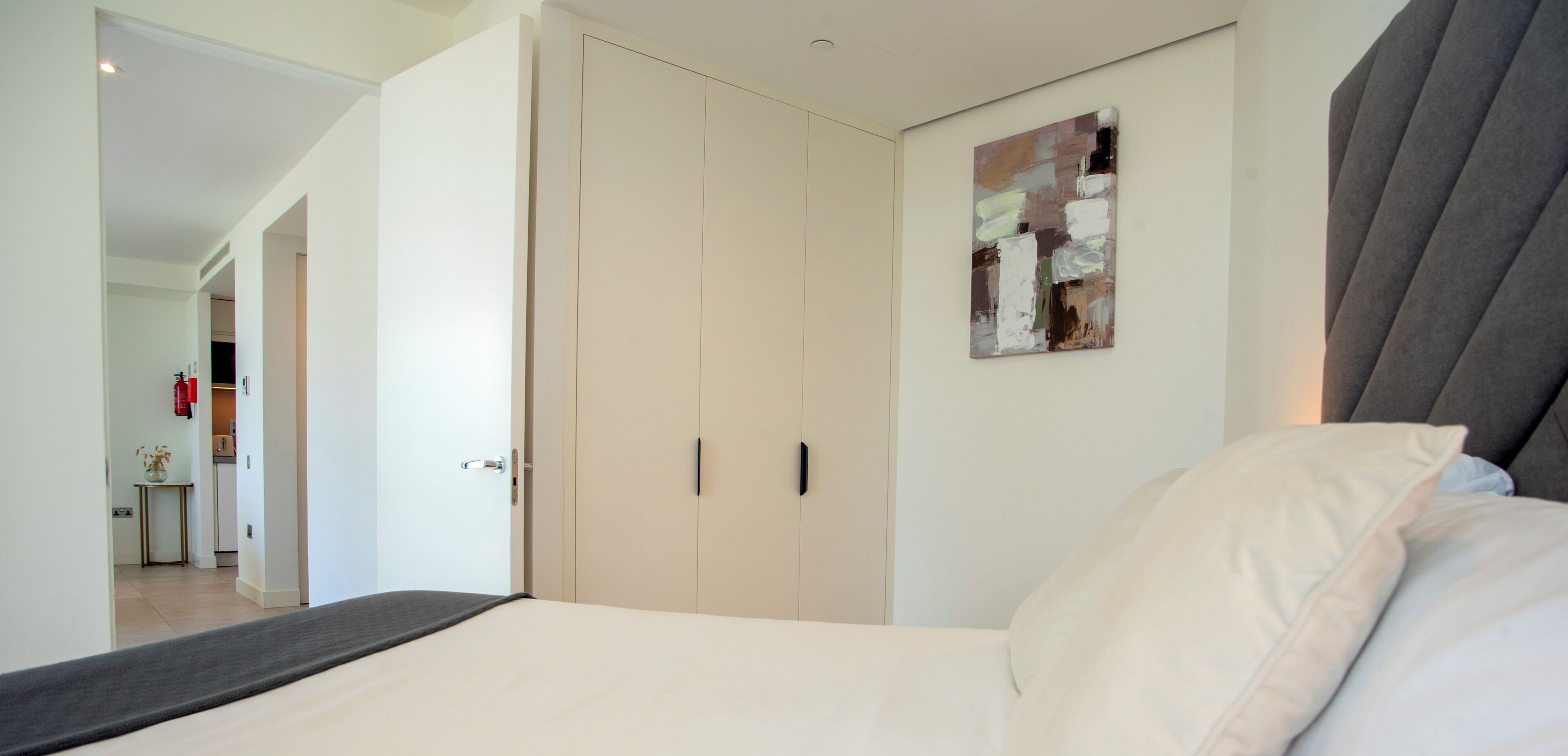 Ein Schlafzimmer mit Bett, einem Schrank, einem Gemälde und einem Flur, der zum Küchenbereich führt.
