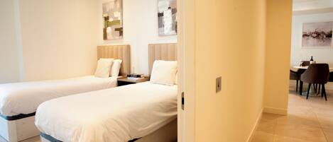 Een hotelkamer met twee éénpersoonsbedden, een tafeltje, een stoel en een bureau met een stoel.