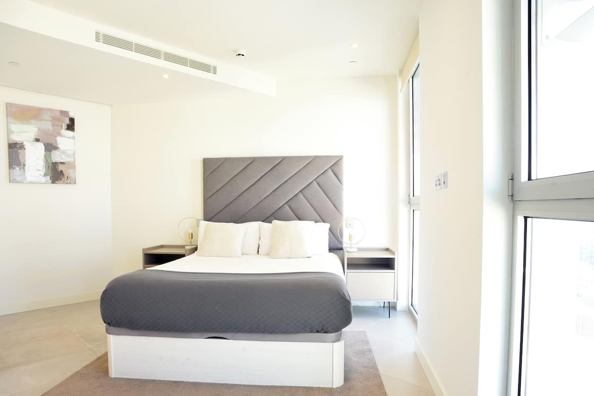 A modern bedroom with a large bed, bedside tables, a headboard, and a window.