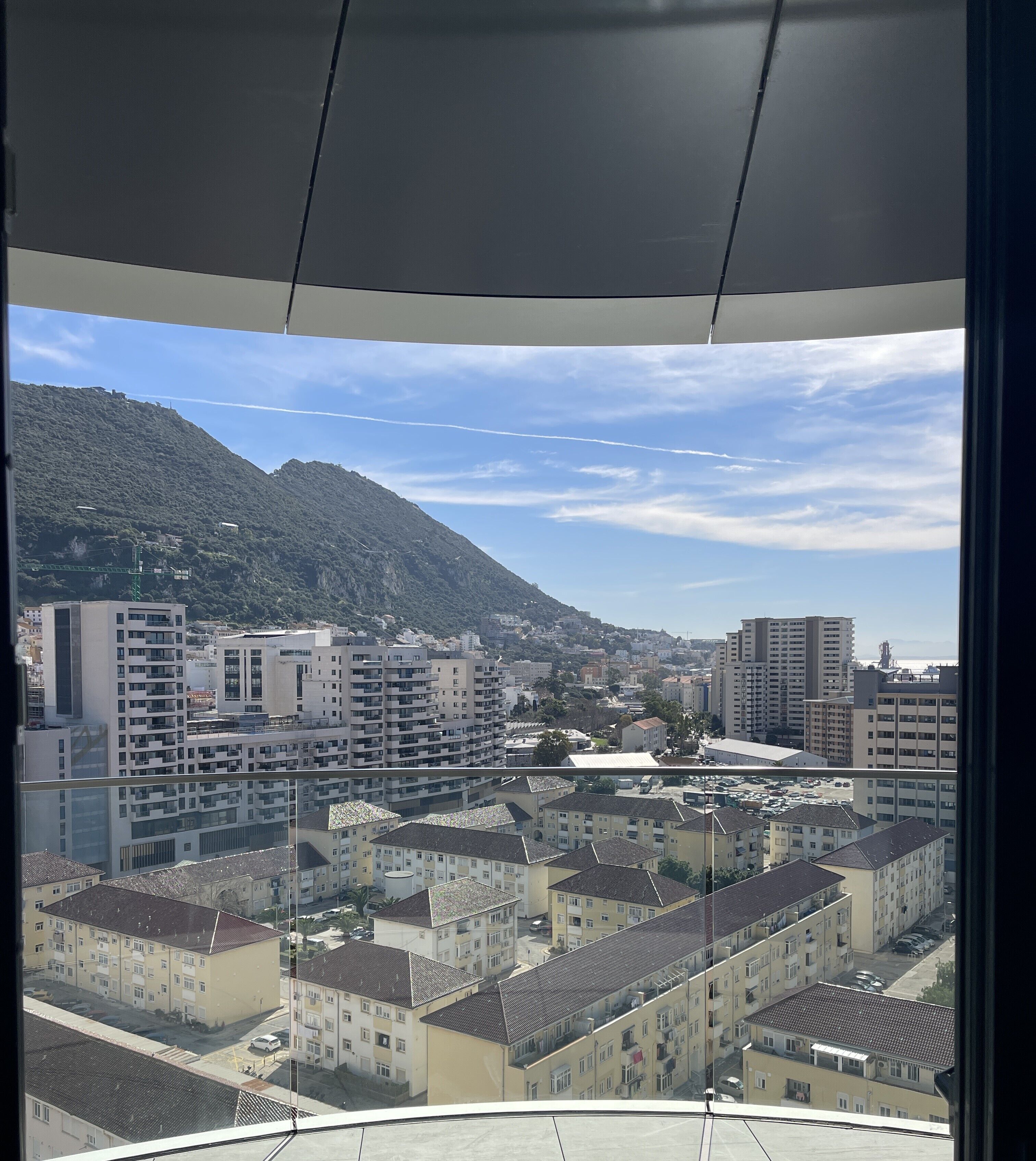 A view from a balcony overlooking a cityscape with multiple buildings, a mountain, and a clear sky.