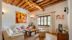 A cozy living room with a wooden ceiling, a large abstract painting, a sofa, a coffee table, and a window with curtains. - New! Villa Can Curreu III - Santa Gertrudis (Ibiza)